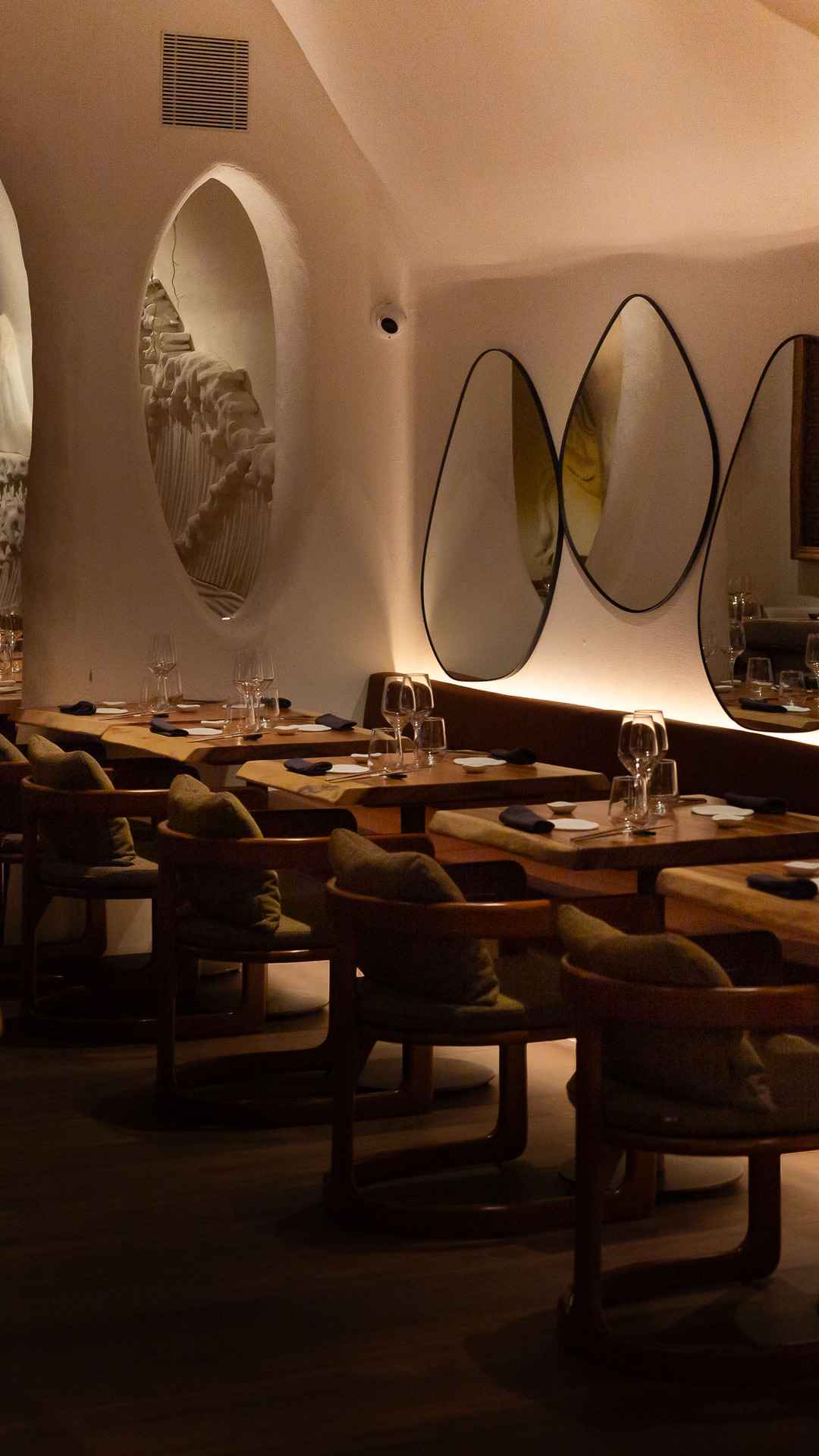 Comedor largo con mesas de nogal, espejos ovalados en la pared y arcos de yeso