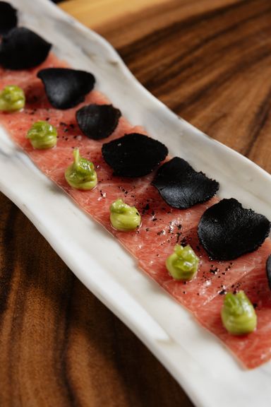 Carpaccio de ventresca con láminas de trufa negra y puntos de crema de aguacate sobre un plato alargado