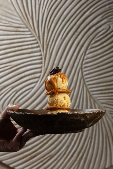 Helado de lúcuma con caramelo en un cuenco de piedra delante de una pared de espirales de yeso