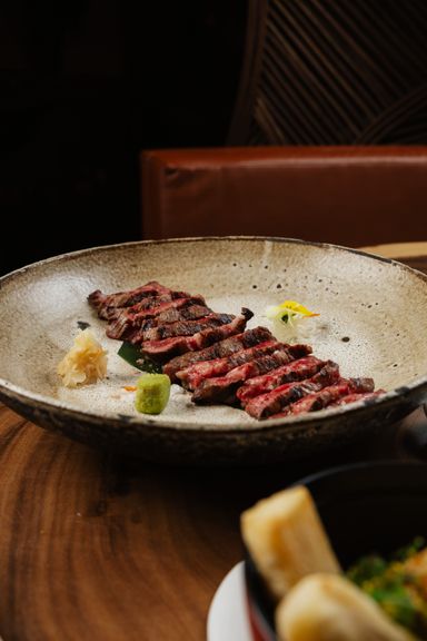 Picanha de wagyu a la brasa laminada en un plato de cerámica, con yuca frita al lado