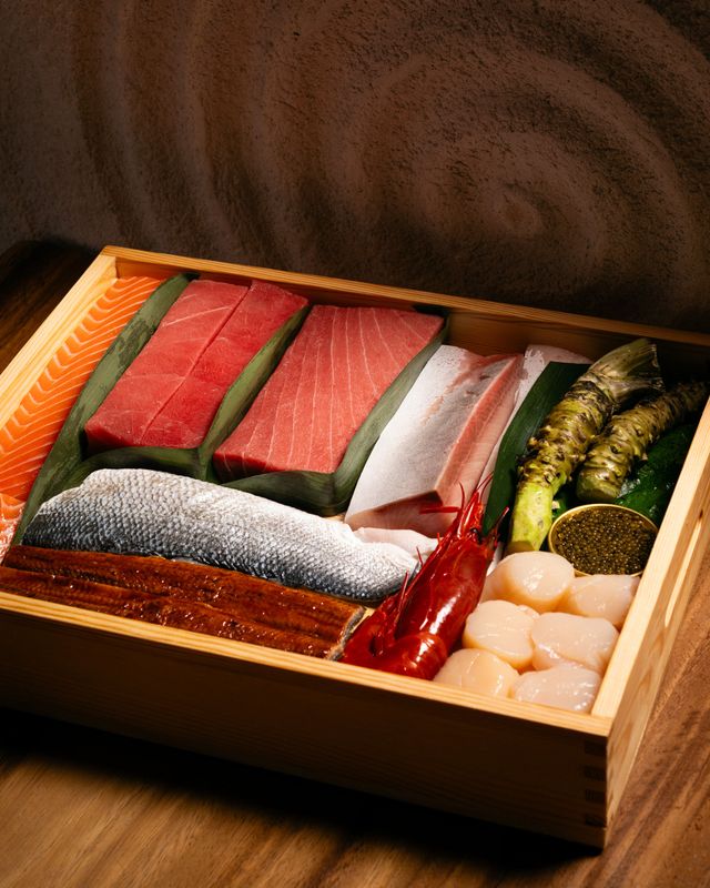 Caja de madera con el producto crudo: atún, ventresca, salmón, lubina, anguila, carabinero, vieiras y wasabi fresco